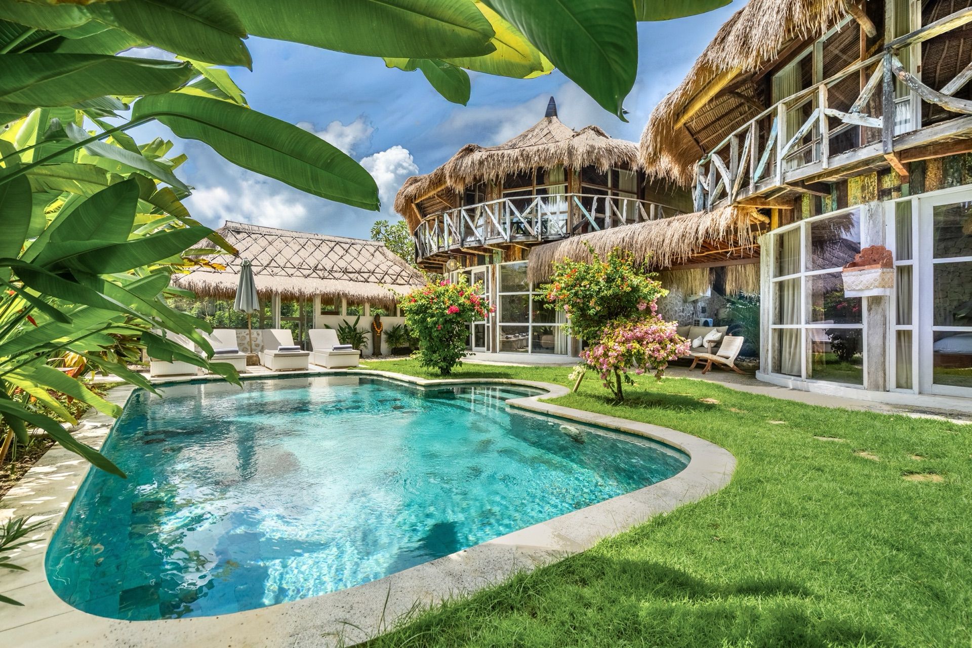 Villa Idaman's freeform pool at the heart of a tropical garden, ringed by two-storey pavilions with thatched alang-alang roofs and flowering bougainvillea