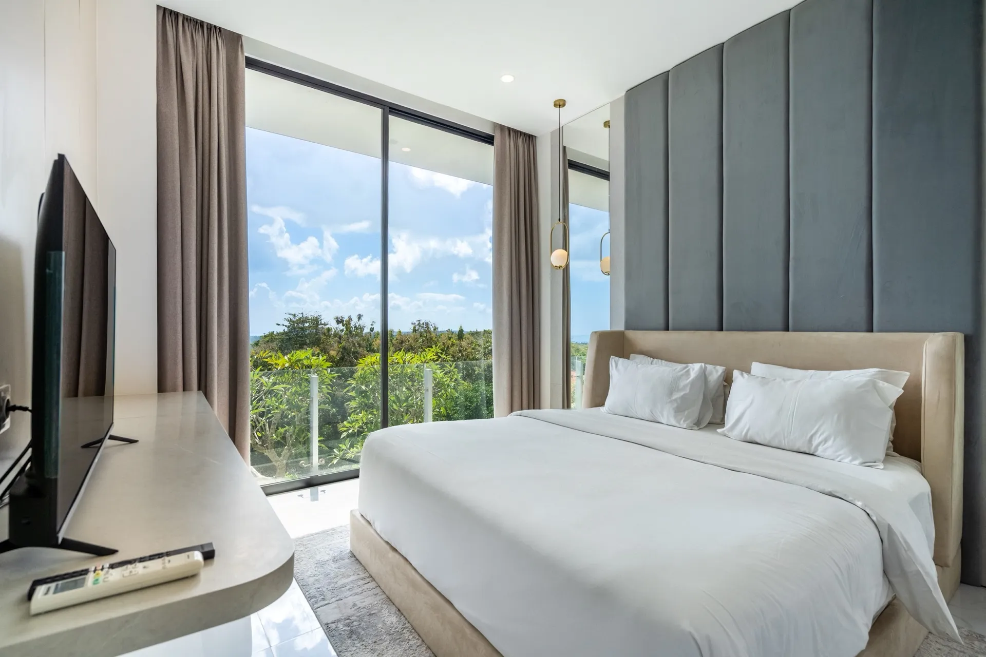 A bedroom at Villa Maisie with a panelled velvet headboard wall and full-height glass to the greenery outside