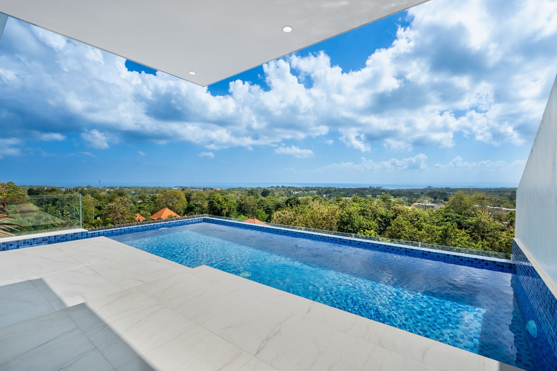 Villa Maisie's blue-tiled pool on the upper terrace, its marble deck looking over the treetops of Bingin towards the sea