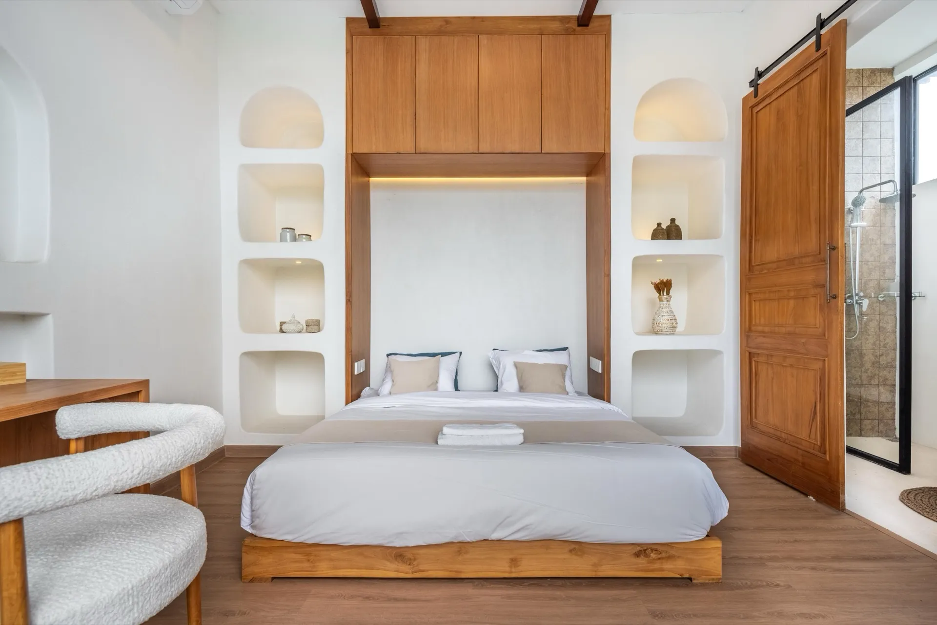 A bedroom at Palm Sugar Villa 4 with a teak platform bed, arched plaster niches and a sliding timber door to the en-suite shower