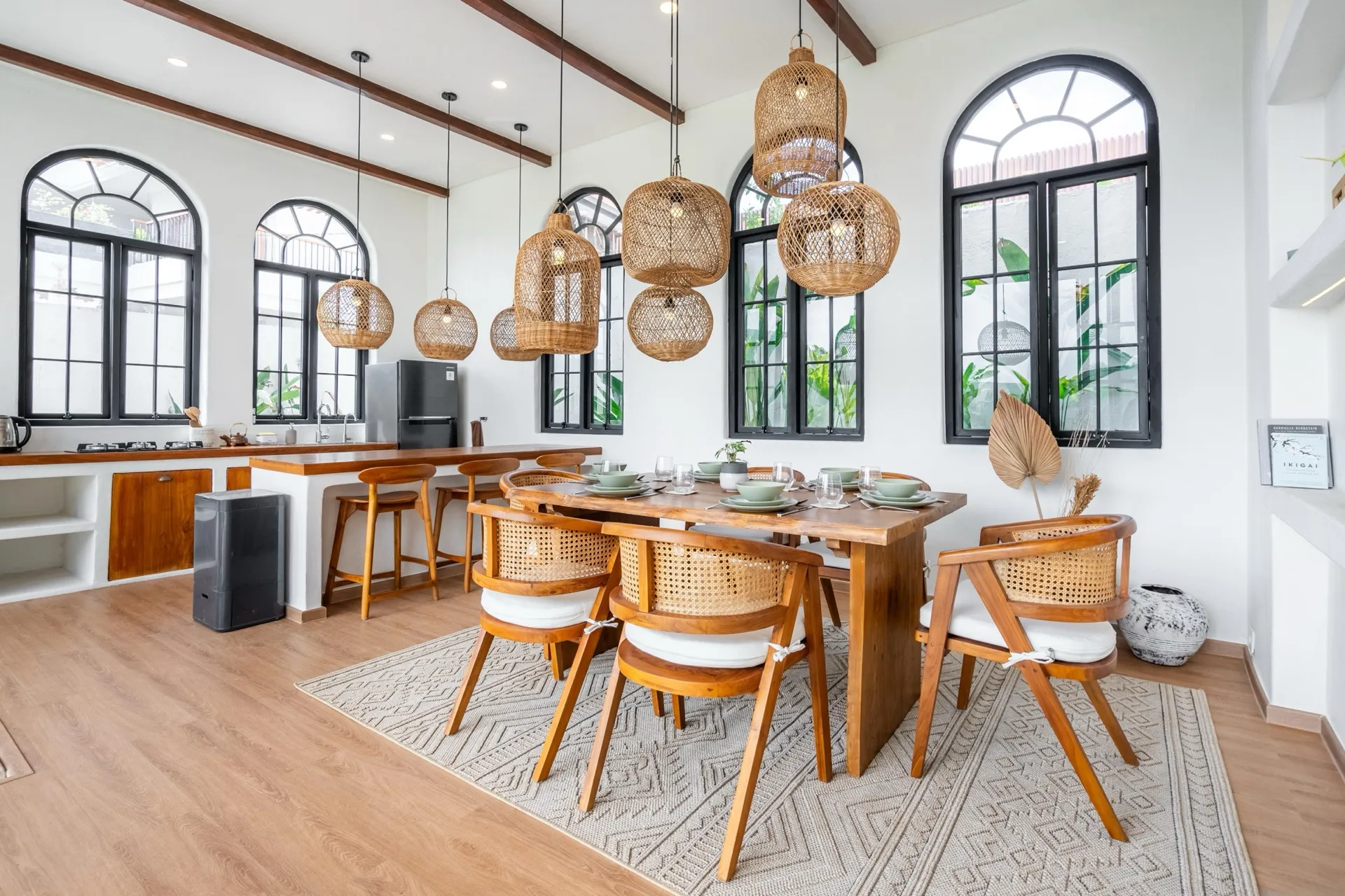 Palm Sugar Villa 4's dining and kitchen space with arched steel-framed windows and a cluster of rattan pendants over the timber table