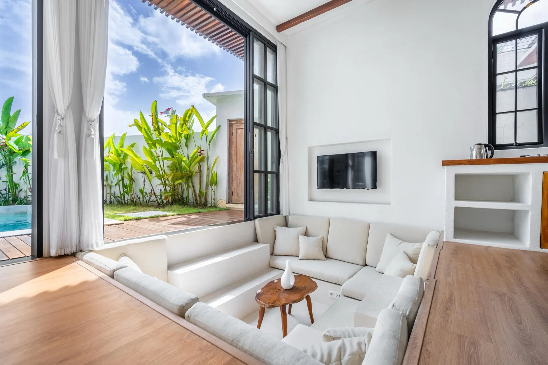 The sunken lounge at Palm Sugar Villa 4, white built-in seating with steel-framed glass doors open to the garden and pool deck