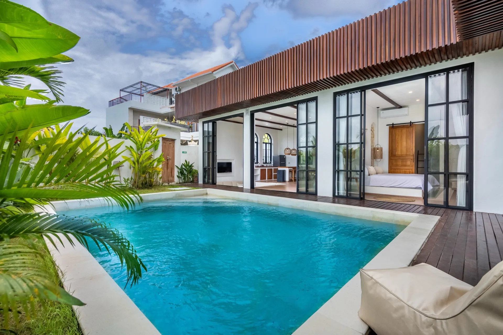 Palm Sugar Villa 4's private pool and timber deck, with steel-framed glass doors opening to the living space and a bedroom beyond