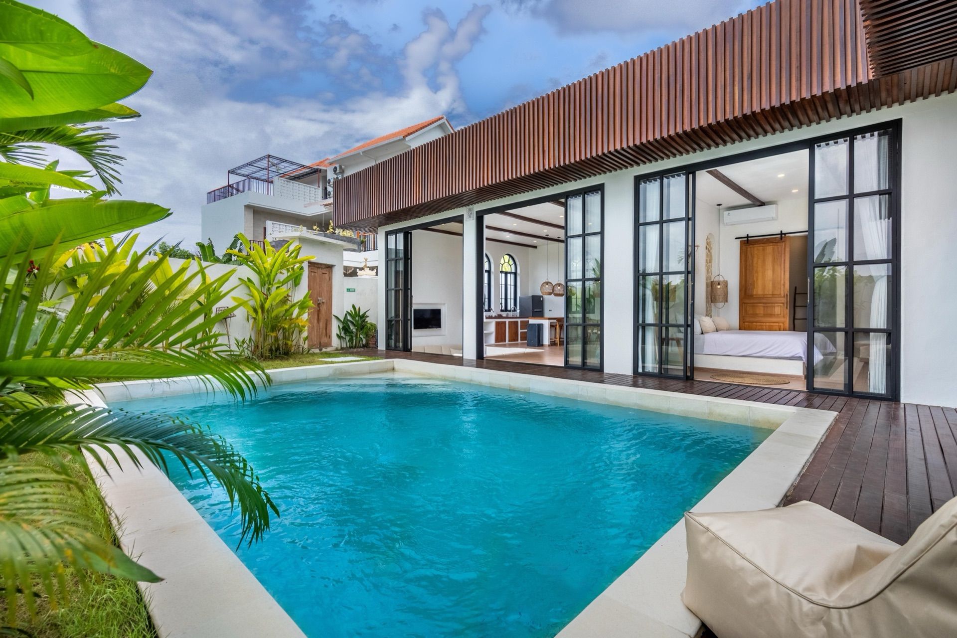 Palm Sugar Villa 4's private pool and timber deck, with steel-framed glass doors opening to the living space and a bedroom beyond